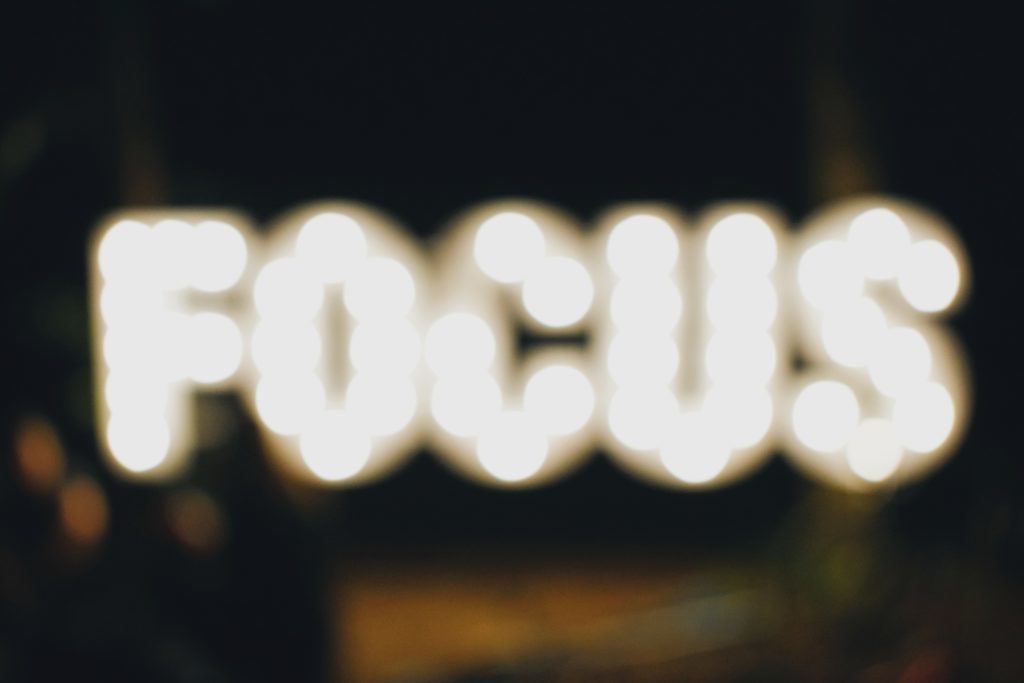 Photo flou d'un panneau lumineux en néon représentant le mot "FOCUS" 