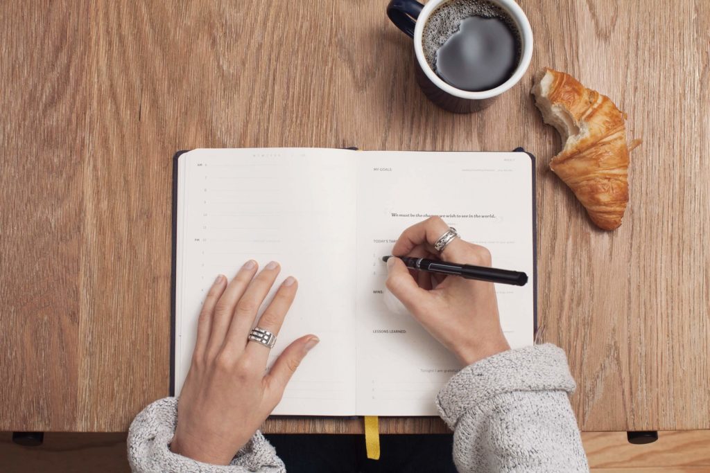 quelqu'un écrit sur un carnet, un café et un croissant